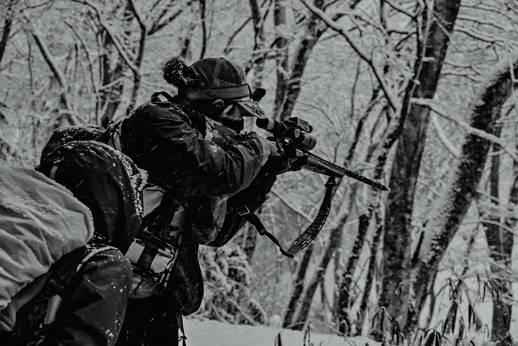 銃を構えスコープを除く狩猟者安田とその様子を見守る参加者