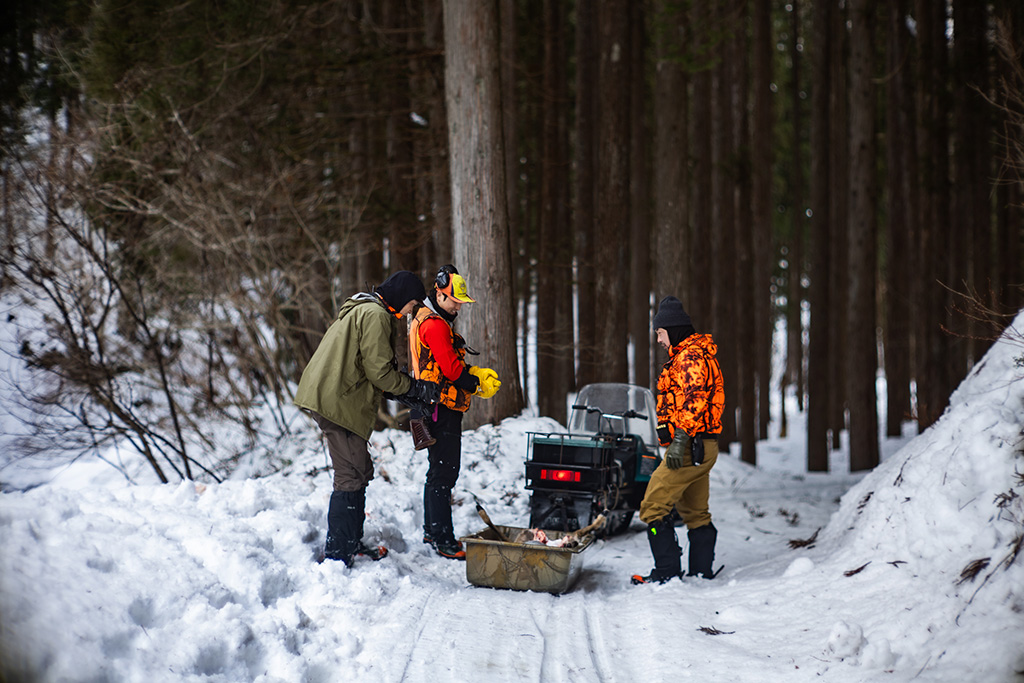 ソリに積んだ鹿を眺める若手猟師3人